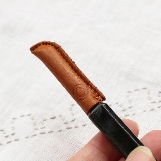 A hand holding a black pen with a brown leather grip, against a white background.