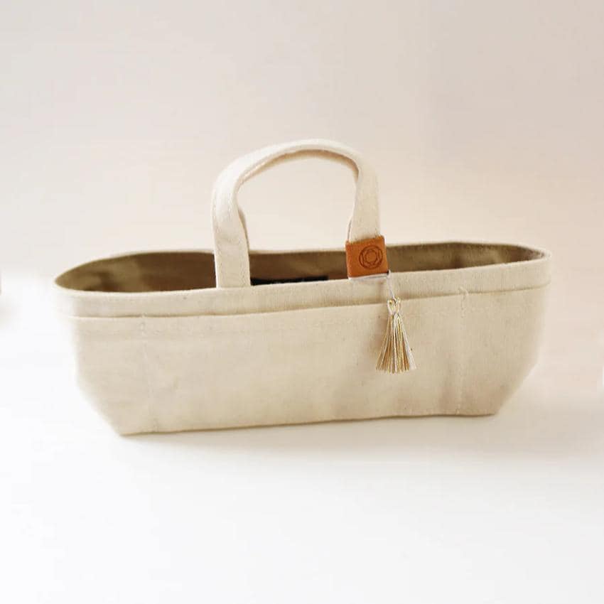 A beige canvas tote bag with a tassel hanging from the handle.