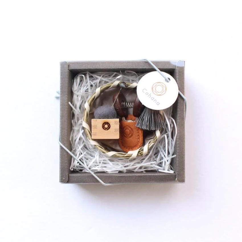 A small, square-shaped gift box containing various items, including a wooden box, a small leather item, and a tassel.