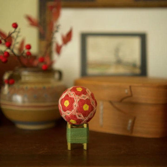 a wooden table with a red and yellow ball on a green stand, a vase with red berries, and a wooden box in the background.