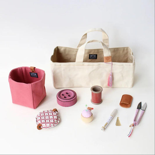 a variety of sewing and crafting supplies, including a beige tote bag, a pink container, a sewing kit, scissors, and other small items.