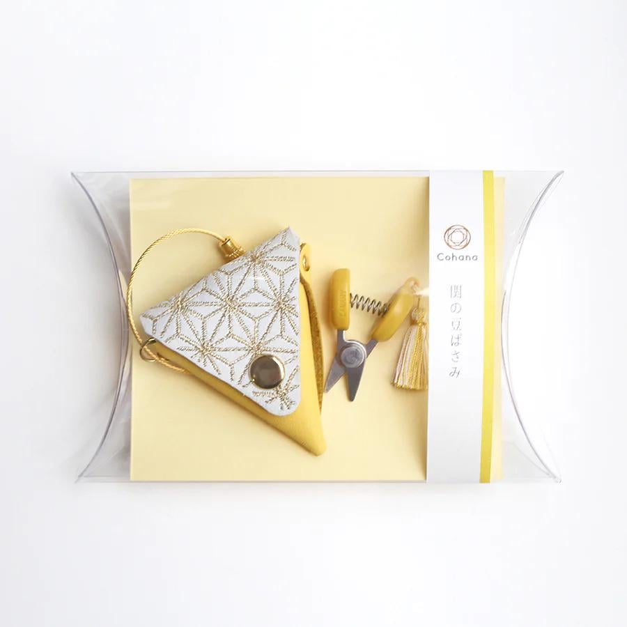 A yellow and white triangular-shaped object with a gold-colored button, accompanied by a pair of scissors and a tassel, all placed on a yellow background.