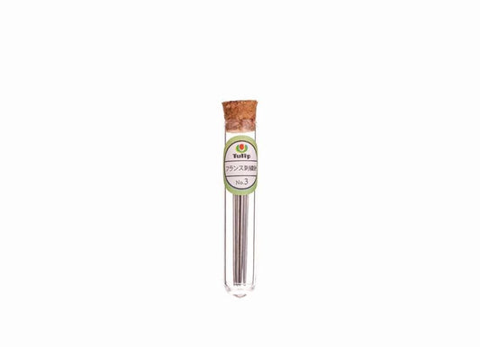 A clear glass tube containing a small amount of a gray substance, with a cork stopper and a label with Japanese text.