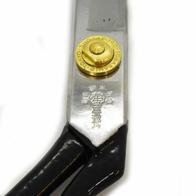 A close-up view of a pair of scissors with a gold-colored screw and a decorative emblem on the handle.