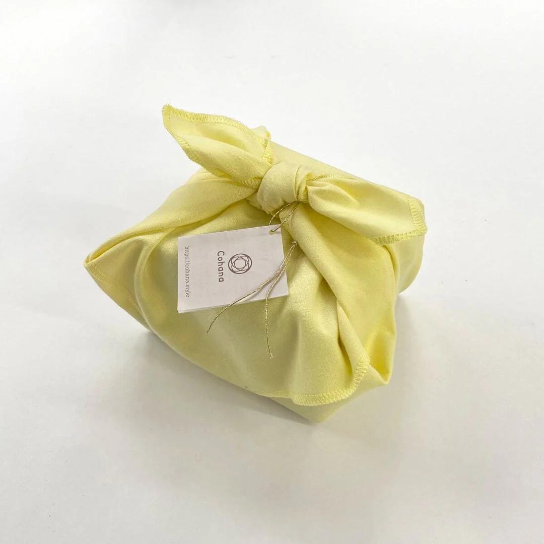 A yellow cloth-wrapped package with a tag attached, sitting on a white surface.
