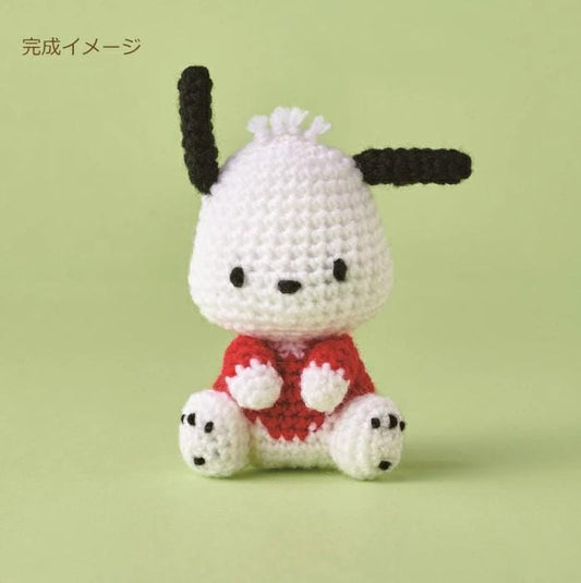 A crocheted toy resembling a small dog or puppy, with a white body, black ears, and a red shirt.