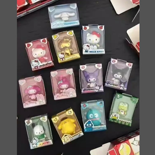 a collection of Hello Kitty figurines and plush toys, each in its own clear plastic packaging. The figurines are arranged on a black surface, with some of them placed in the center and others surrounding them. The packaging features the Hello Kitty character and the text "Hello Kitty" prominently displayed.