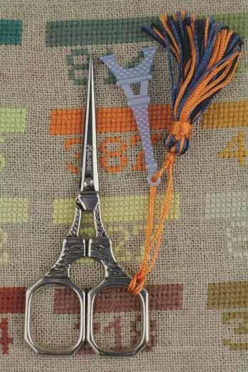 A pair of silver scissors with a tassel attached, placed on a colorful fabric background.