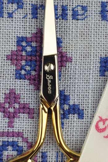 A close-up view of a pair of gold-colored scissors resting on a blue and purple embroidered fabric.