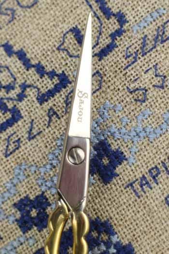A pair of scissors with the brand name "Sterling" printed on the handle is shown against a background of blue and white embroidered patterns.