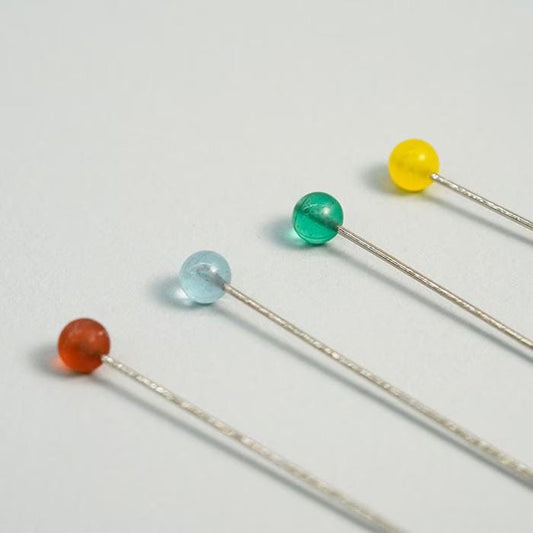 Four colorful beads on a white background, each attached to a silver pin.