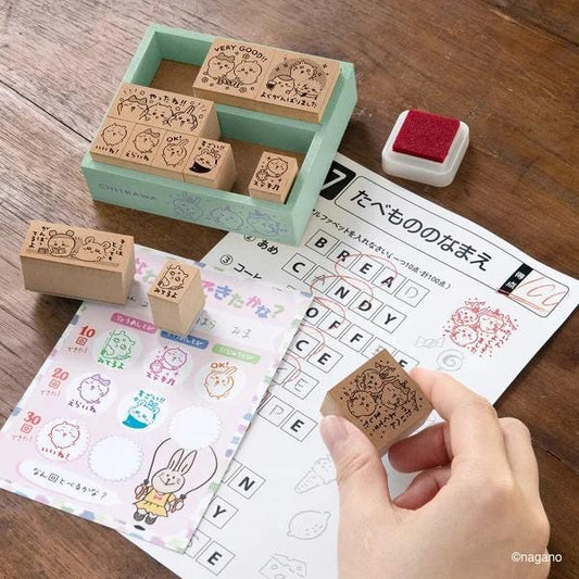 a hand holding a stamp, surrounded by various items such as a stamp holder, a sheet of paper, and a puzzle.