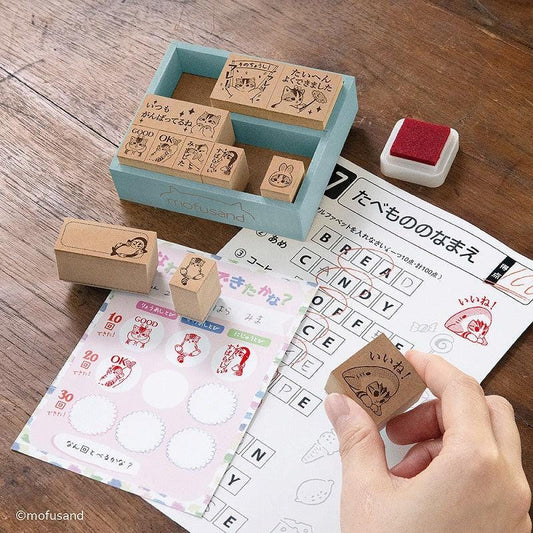 a hand holding a stamp, surrounded by various items such as a blue stamp holder, a sheet of paper with a crossword puzzle, and a stack of stamps.