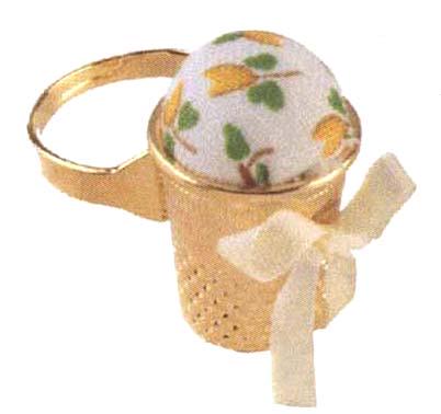 A gold-colored tea strainer with a white and green floral pattern on it, tied with a white ribbon.