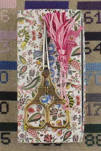 A pair of gold scissors with a pink tassel is placed on a white and pink floral patterned box.