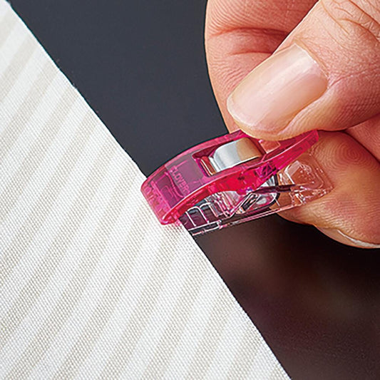 A hand is holding a pink plastic clip, which is being used to hold a piece of fabric or material together.