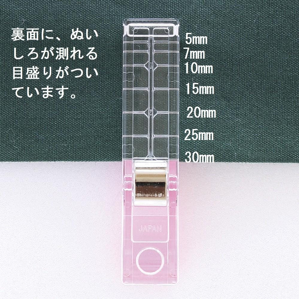 A clear plastic ruler with measurements in millimeters, labeled from 5mm to 30mm, is shown against a green fabric background.