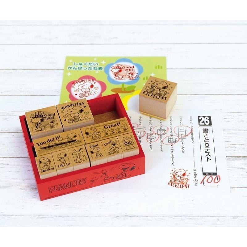 A set of Peanuts-themed rubber stamps, including a larger stamp and a smaller stamp, along with a box and a sheet of paper.