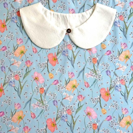 a white collar with a button, set against a background of a blue fabric adorned with a floral pattern.