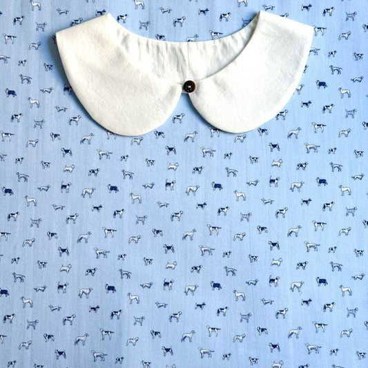 a white collar with a button, placed on a blue fabric with a repeating pattern of small white dogs.