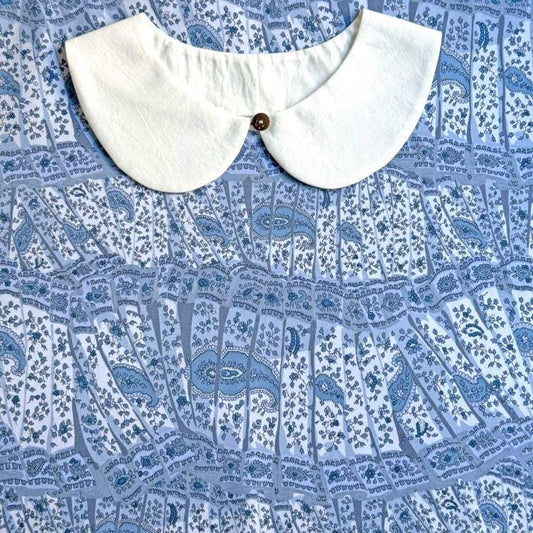 a white collar with a button, placed on a blue and white patterned fabric.
