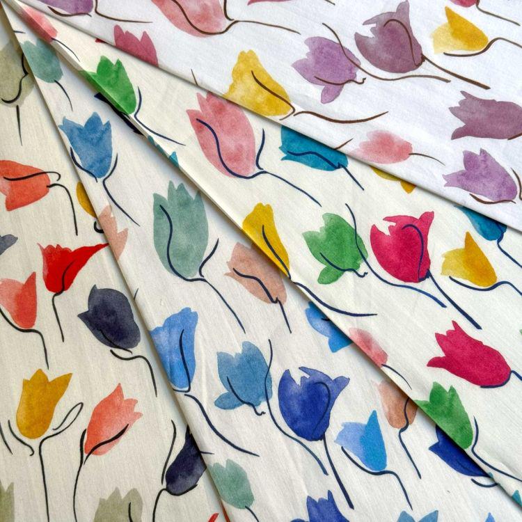 The image is a close-up of a fabric with a repeating pattern of colorful flowers, including red, yellow, blue, and green flowers.