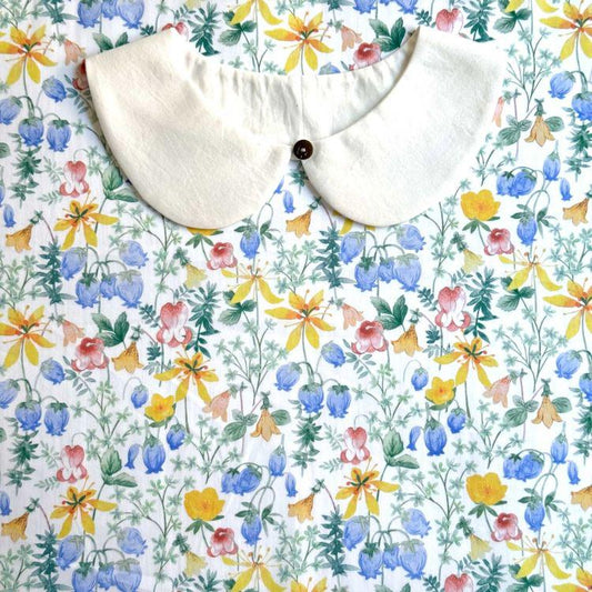 a white collar with a button, placed on a fabric with a colorful floral pattern.