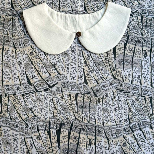 a white collar with a button, placed on a patterned fabric with a repeating black and white design.