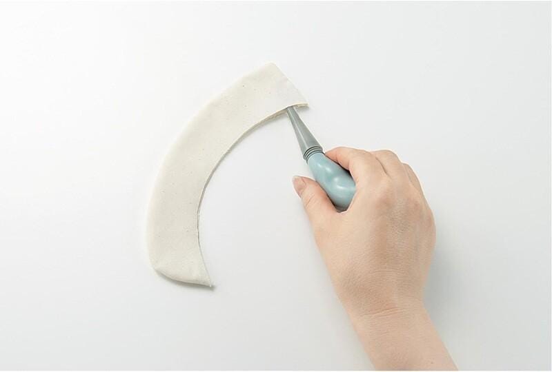 A hand is using a blue tool to cut a white fabric or material, which appears to be a piece of cloth or fabric.