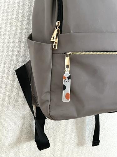A gray backpack with a cat-themed keychain attached to the zipper pocket.