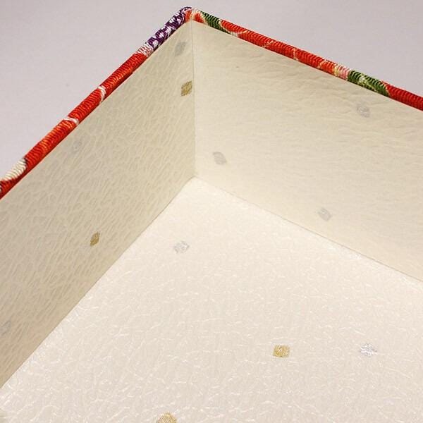 a white box with a red and green patterned border, and small gold dots on the surface.