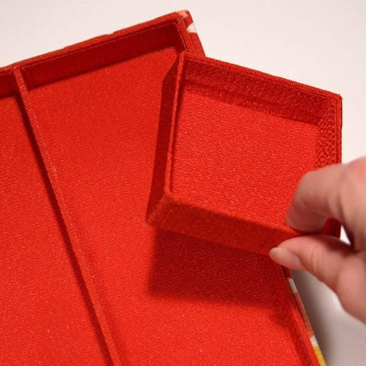 A hand is holding a red box with a matching lid, which is placed on a white surface.