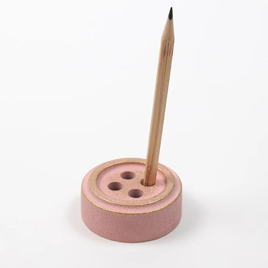 A pink button-shaped pencil holder with a wooden pencil inserted in it.