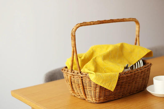 A wicker basket with a yellow cloth and silverware is placed on a wooden table.