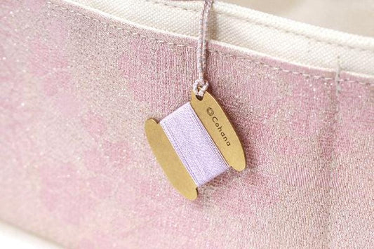 A gold-colored spool of thread with a pink spool attached to it, hanging from a white fabric surface.