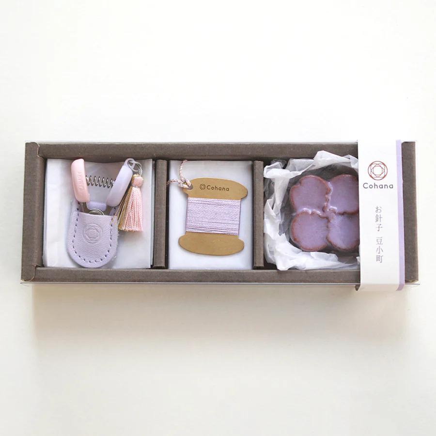 A set of three small items, including a keychain, a spool of thread, and a small purple object, all placed in a brown box with a white label.