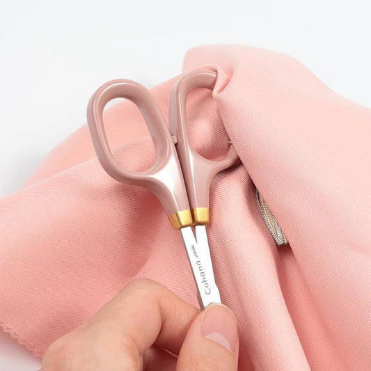 A hand holding a pair of pink scissors with the blades open, resting on a pink fabric.
