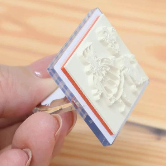 A hand is holding a white stamp with a floral design on it.