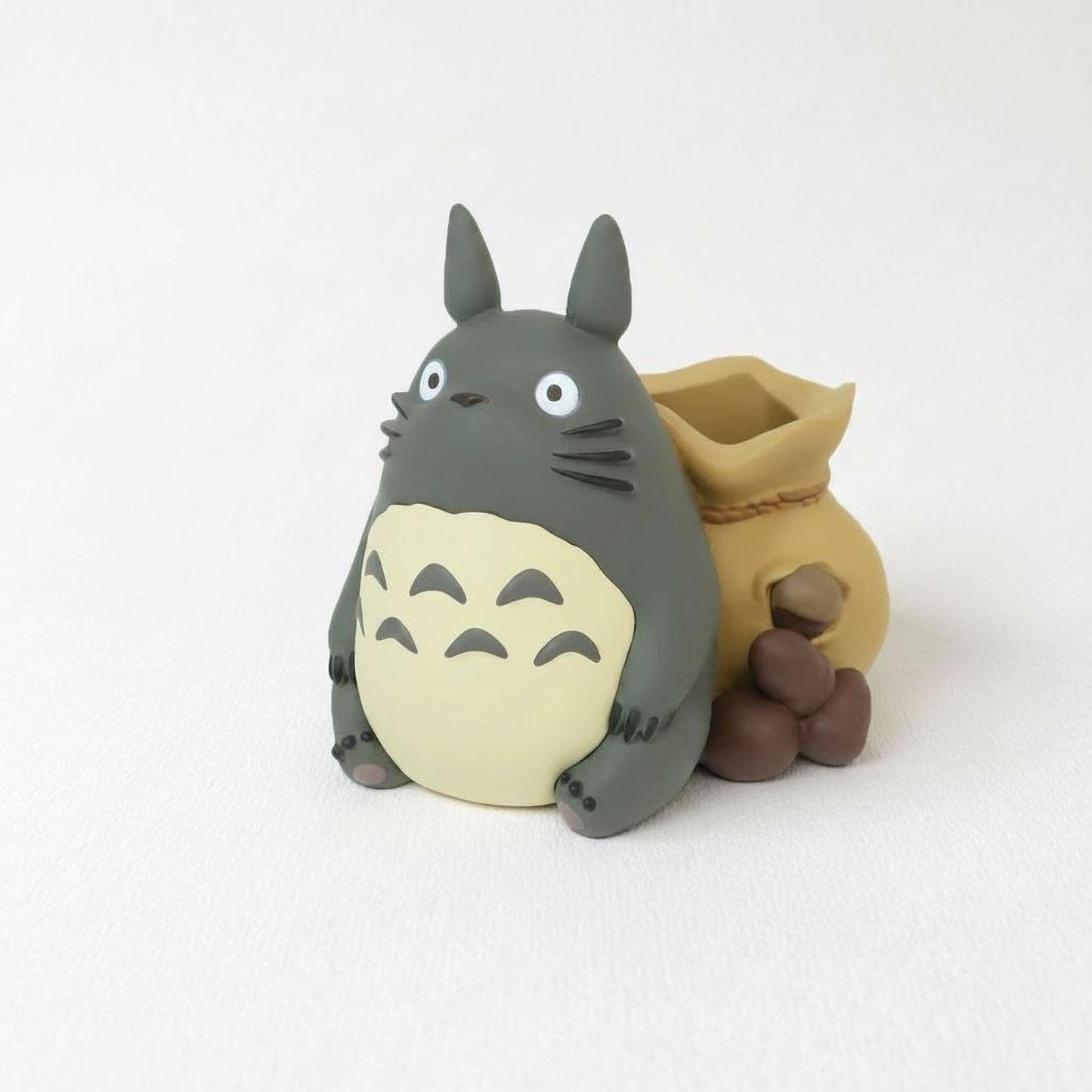A figurine of a cat-like creature with a gray body and yellow accents, sitting next to a small bag of what appears to be nuts or other small items.