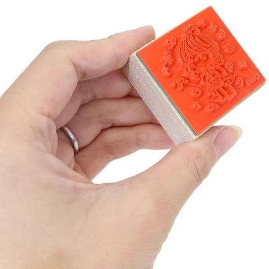 A hand holding a red stamp with an image of a person on it.