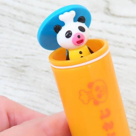 A small toy panda wearing a chef's hat is sitting inside an orange tube with a red and white design.