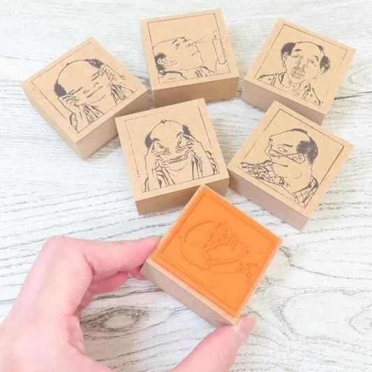 A hand is holding a square stamp with an image of a person's face on it, surrounded by other similar stamps.