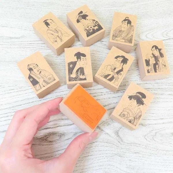 A hand is holding a stamp with an orange background, surrounded by several other stamps featuring black and white illustrations of people.