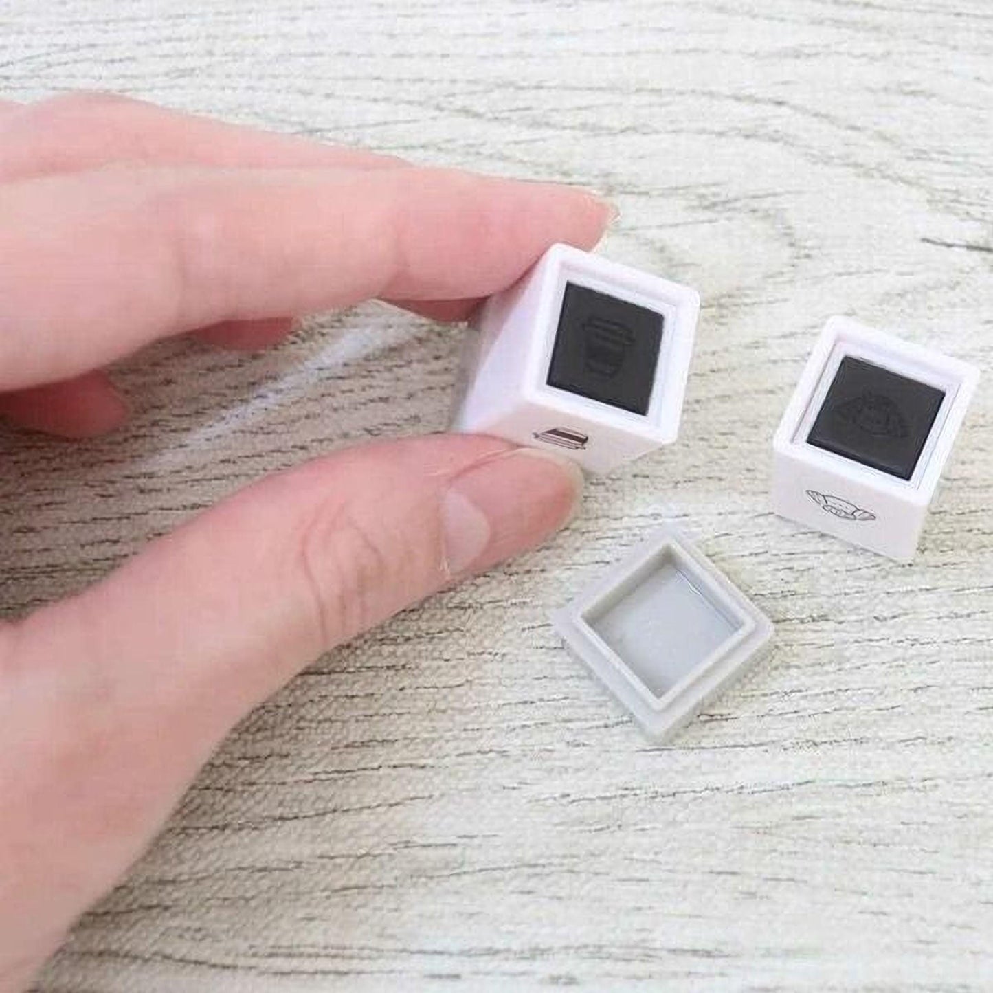 A person's hand is holding two small white square objects with black markings on them, which appear to be some sort of decorative or functional items.