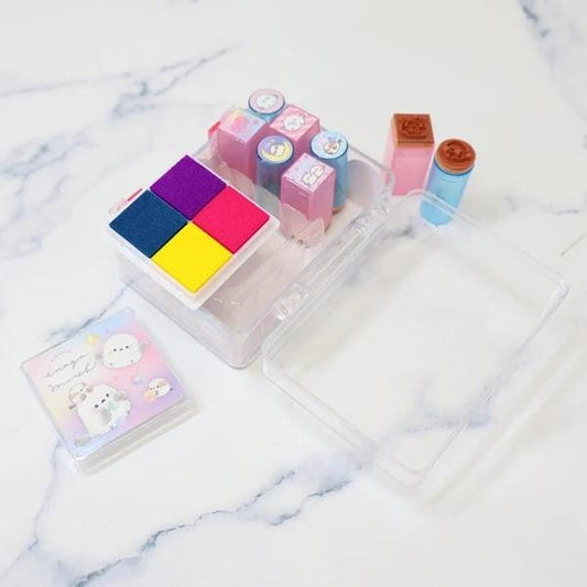 A clear plastic container with various colorful stamps and a small card with cartoon characters on it, all placed on a marble surface.