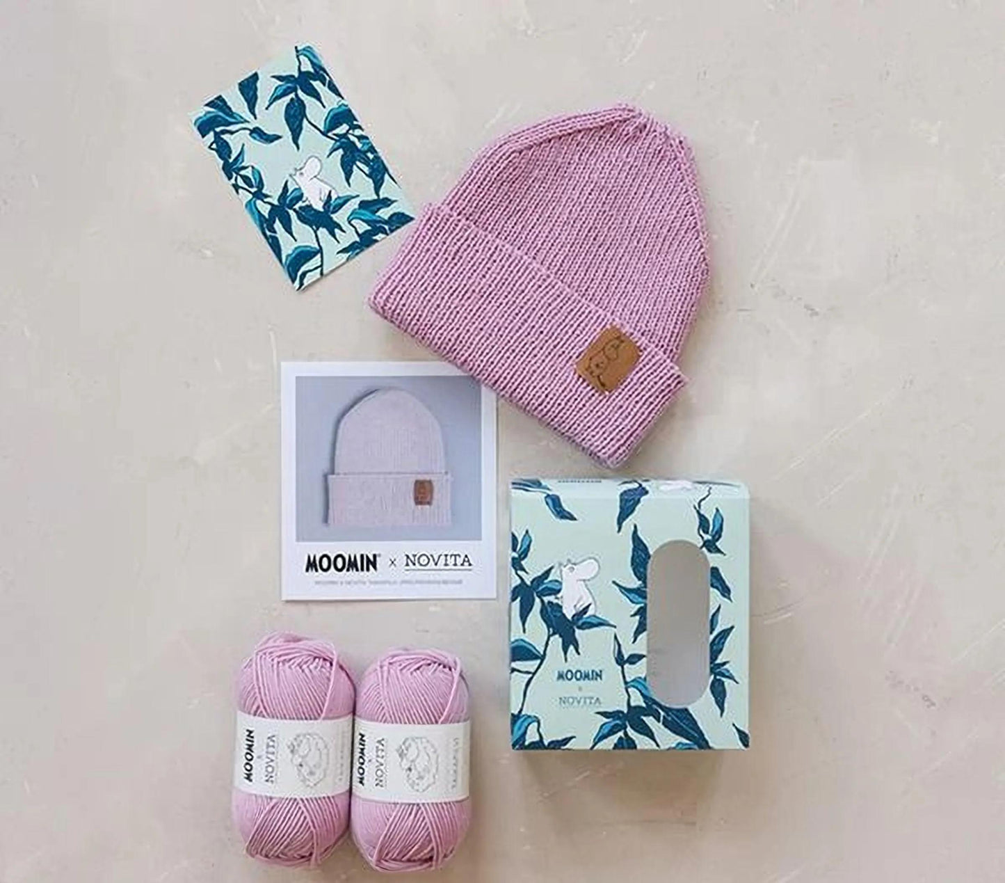 various knitwear items and yarn, including a pink knit hat, two balls of yarn, and a box with a floral pattern.