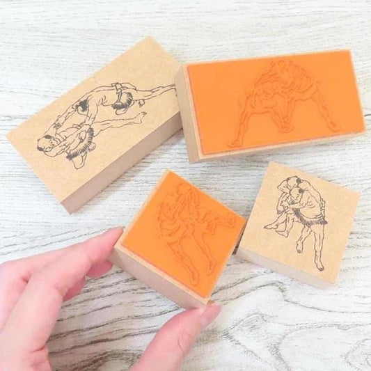 a hand holding a small orange stamp with a black and white illustration of a couple embracing.