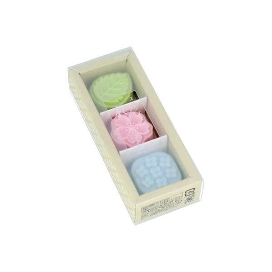 A rectangular box containing three small, colorful objects, likely a set of three different colored candles or small decorative items.