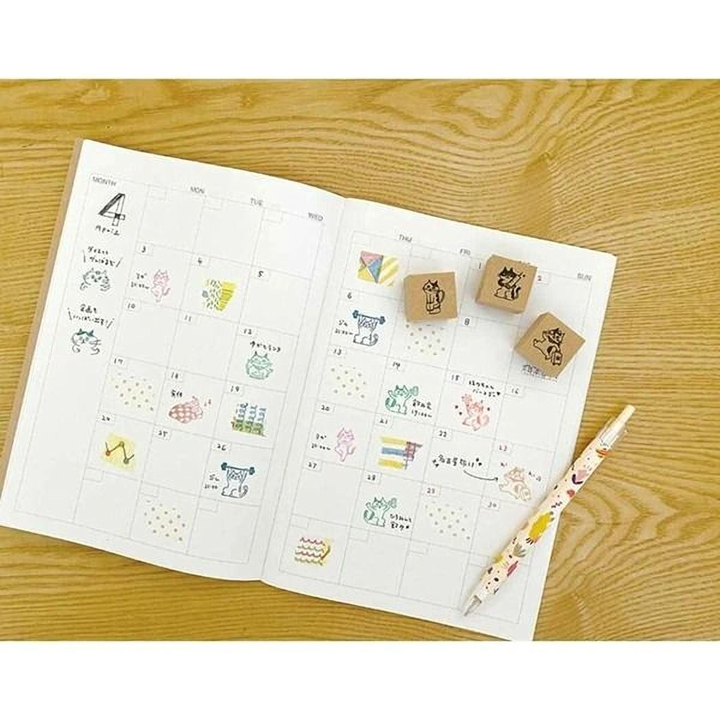 an open notebook with a calendar page, a pen, and two wooden stamps on a wooden surface.