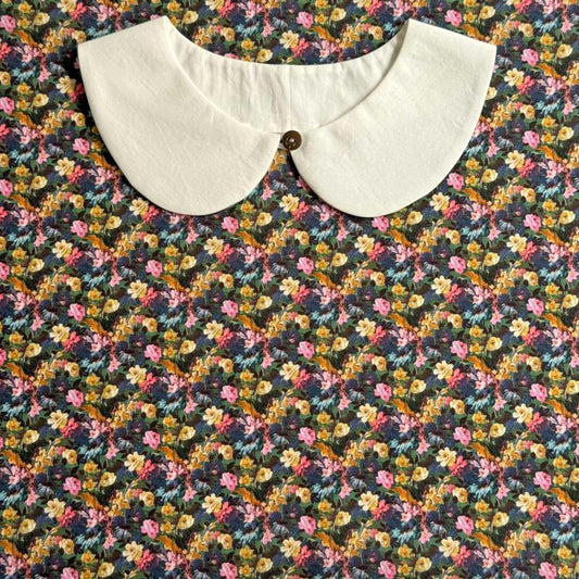 a white collar with a button, set against a colorful floral print background.